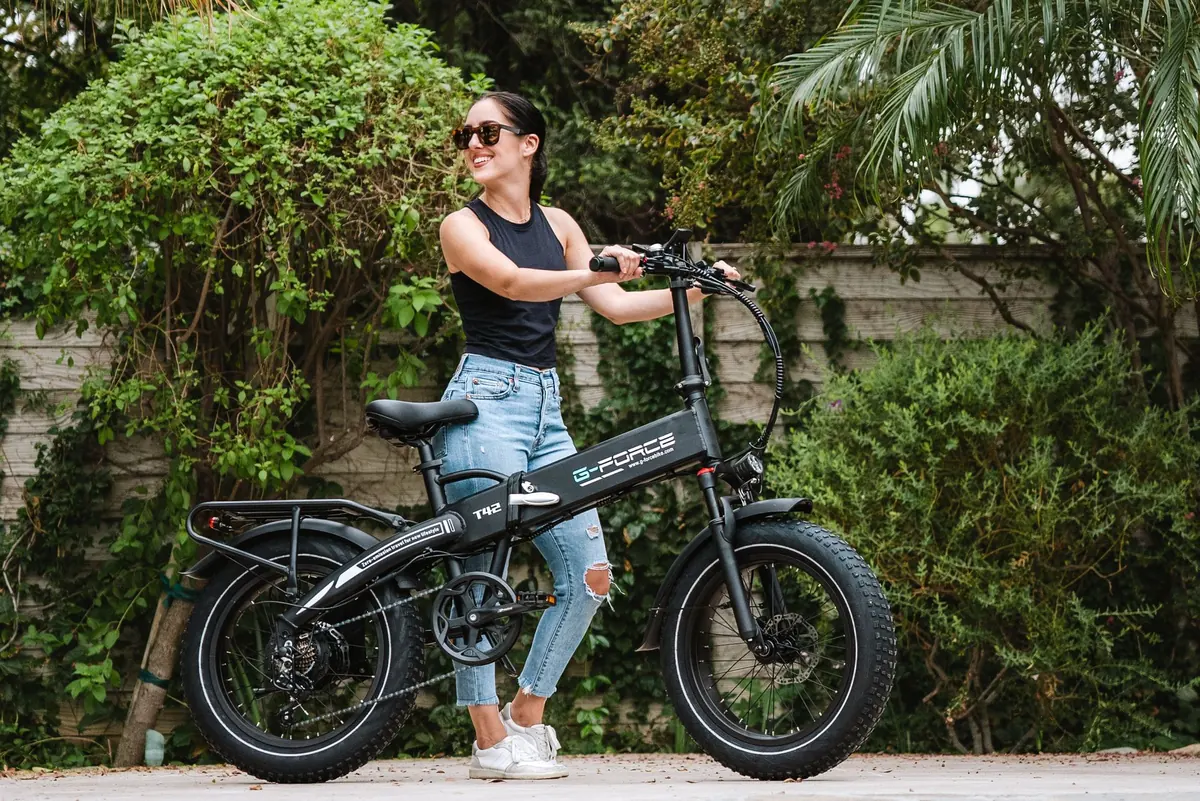 A cyclist taking a pause beside an electric bicycle in a leafy setting. Editorial lifestyle photograph.